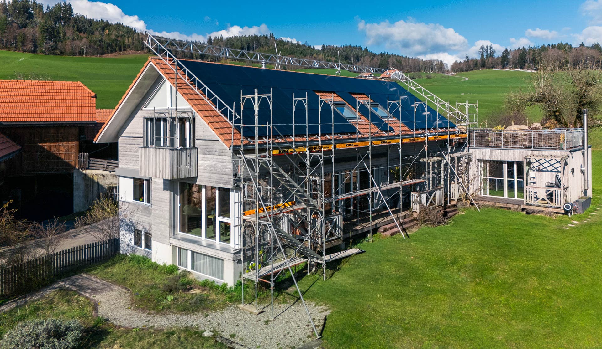 Einfamilienhaus mit vollflächiger Photovoltaik-Anlage auf dem Schrägdach, Fassadengerüst entlang der Traufe und Schutzkonstruktion über den Dachrand